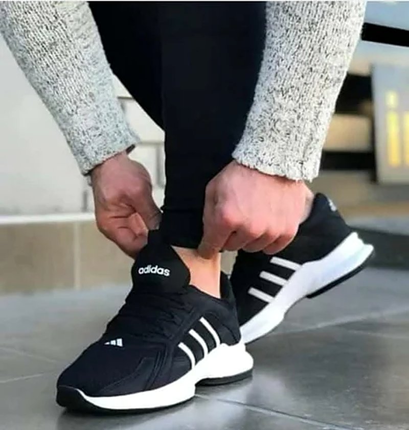 Black sneakers with white stripes, worn with black trousers